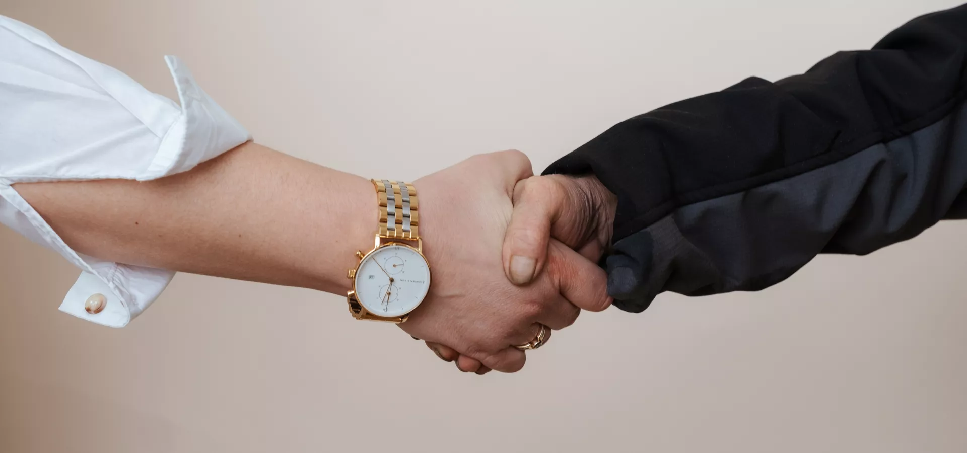 Eine Frau und ein Mann geben sich die Hand. Es sind nur die Hände bis zu den Ellenbogen zu sehen. 